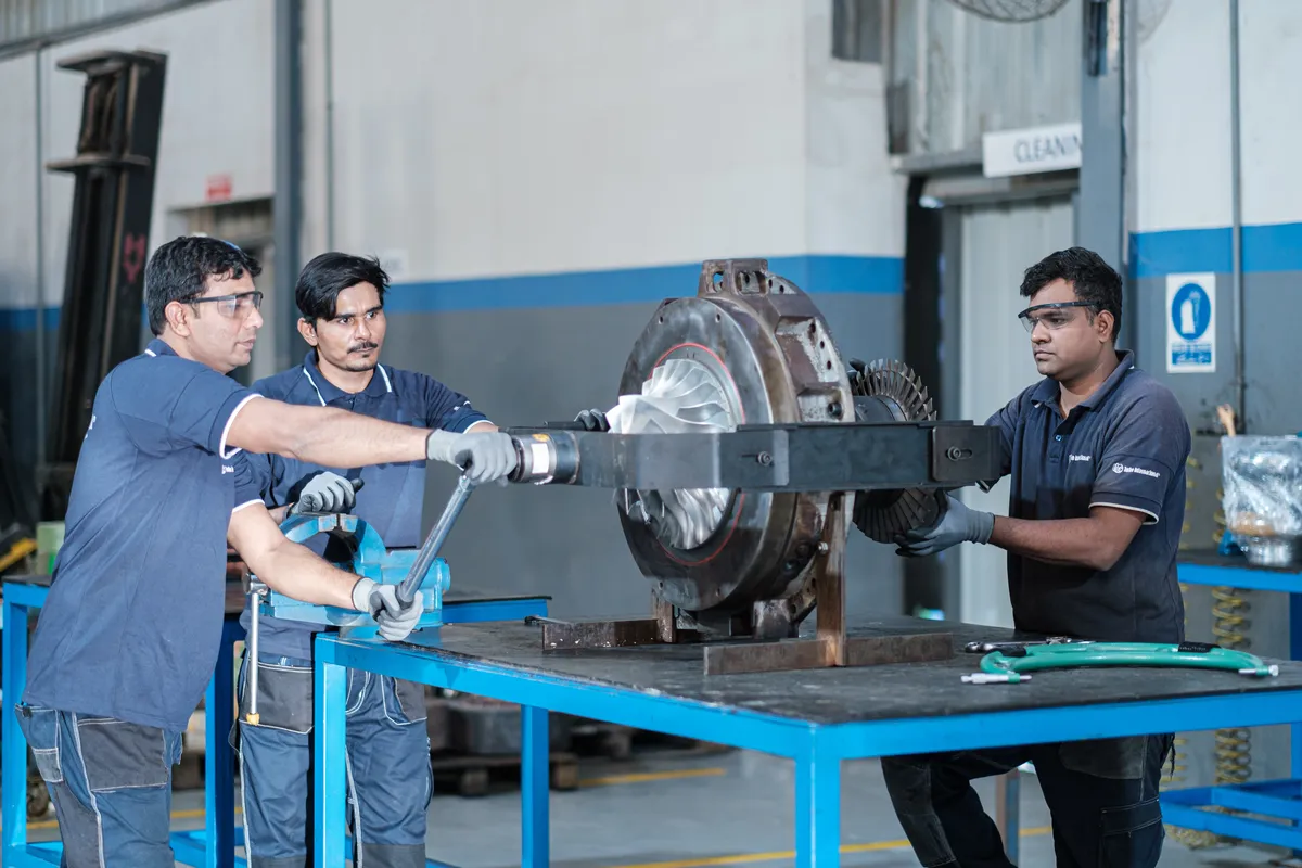 Three technicians handling a turbocharger rotor at the Karachi workshop