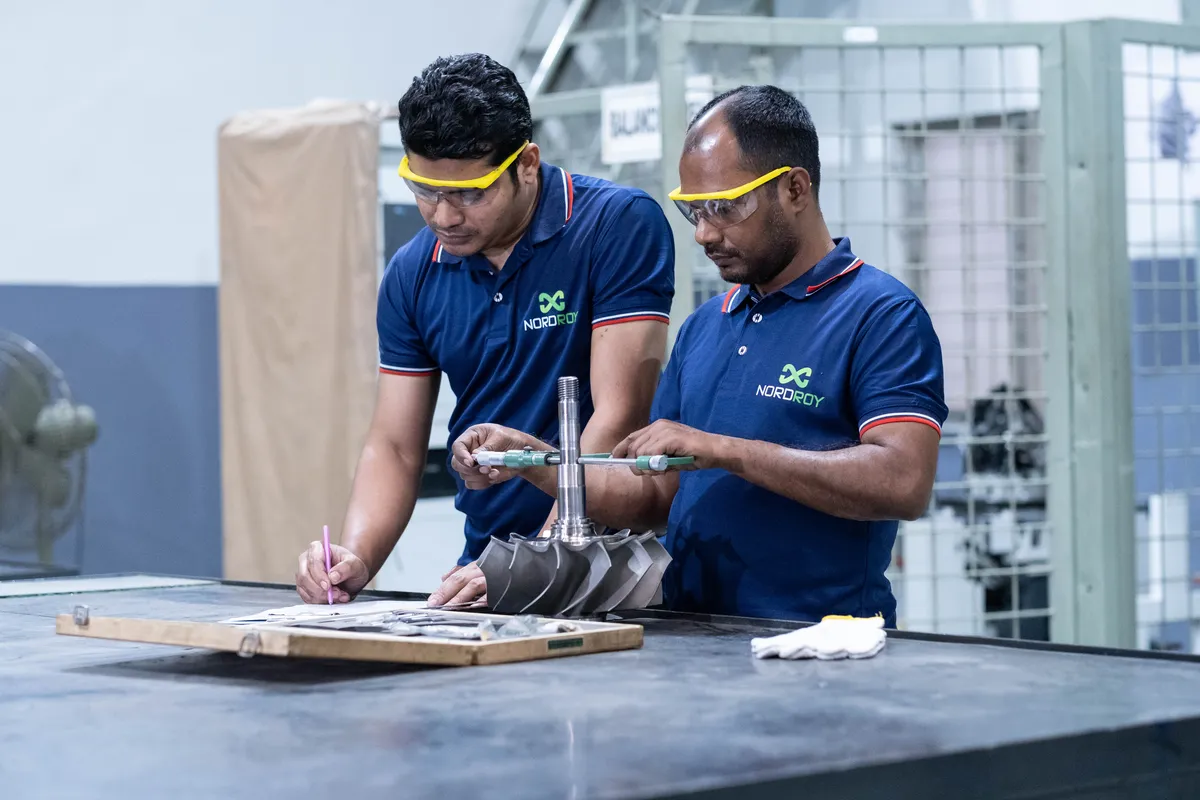 Two technicians measuring and recording a turbocharger rotor at Dhaka